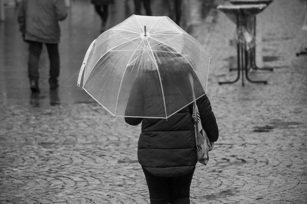 portrait of woman walking with transparent umbrella in the pedestrian street - Fotó, kép