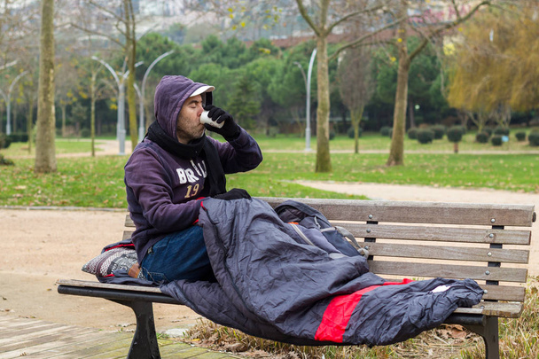Hombre sin hogar está bebiendo café en el banco
 - Foto, imagen