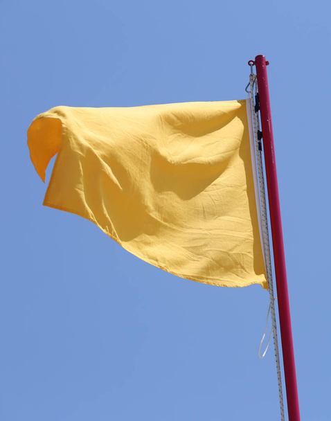 Iso keltainen lippu vilkuttaa hälyttää huomiota sininen taivas tausta
 - Valokuva, kuva
