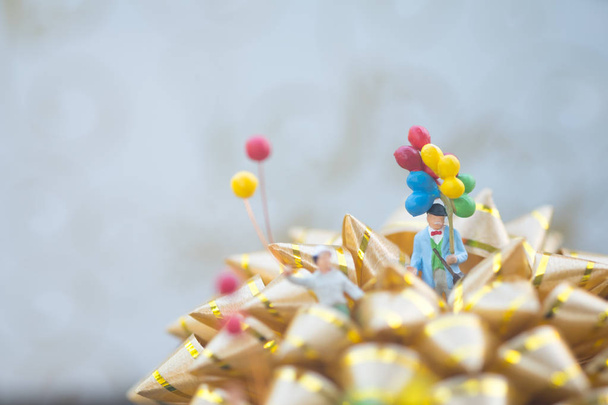 Μινιατούρα άτομα που κατέχουν με μπαλόνι στέκεται στο χρυσό τόξο. Καλά Χριστούγεννα και Ευτυχισμένο το νέο έτος έννοια. - Φωτογραφία, εικόνα