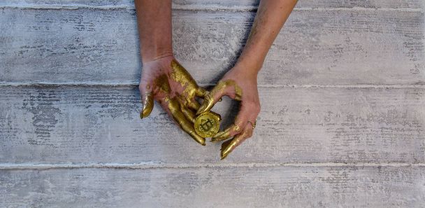 Women's hands painted with gold paint hold golden bitcoin - Fotoğraf, Görsel
