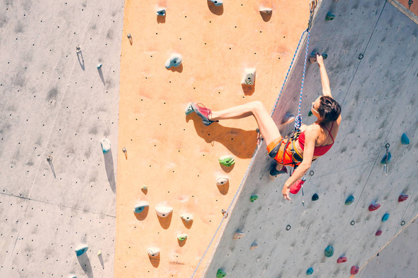 Entrenamiento en el gimnasio de escalada. Una mujer fuerte sube a una ruta de escalada en terreno artificial. Chica delgada involucrada en deportes
. - Foto, imagen