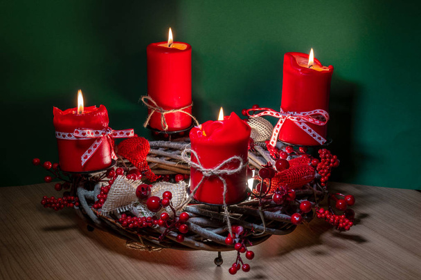 Σύγχρονη Χριστουγεννιάτικο στεφάνι με τέσσερα κόκκινα κεριά σε ξύλινη επιφάνεια με πράσινο φόντο - Φωτογραφία, εικόνα