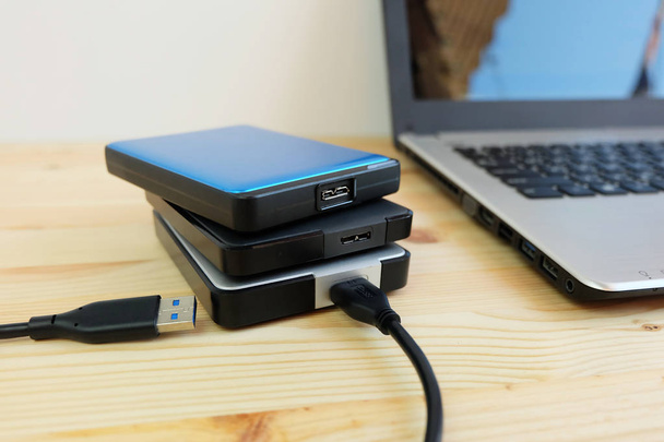 Mnoho barevné přenosné externí pevné disky USB 3.0 připojení k notebooku na dřevěné pozadí - Fotografie, Obrázek