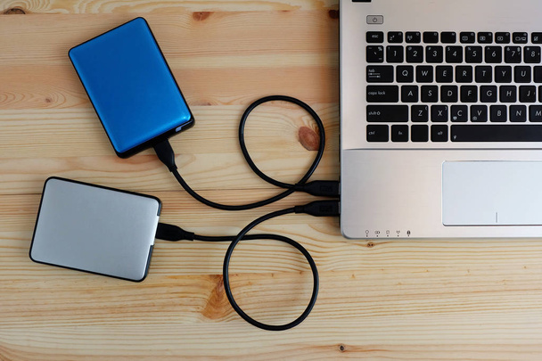 Molti hard disk esterni portatili colorati USB3.0 si collegano al computer portatile su sfondo di legno
 - Foto, immagini