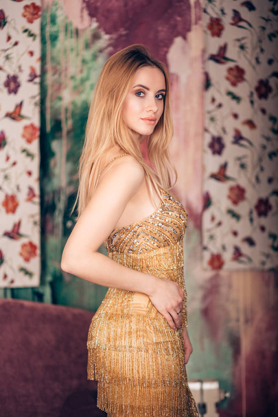 Porträt einer eleganten schönen Frau im Studio. Das blonde Mädchen zieht ein goldglänzendes Kleid an und blickt in die Kamera. Mode, Glamour, Luxus, Partykonzept - Foto, Bild