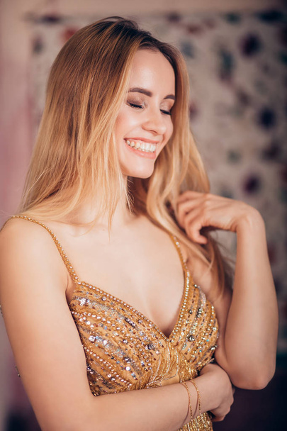 Beautiful young woman in Golden dress laughing, smiling indoors. Positive human emotions, happiness, joy, facial expression, party, holiday concept - Photo, Image