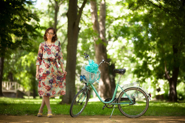 girl standing infornt of vintage bicycle on a road in the park - Fotoğraf, Görsel