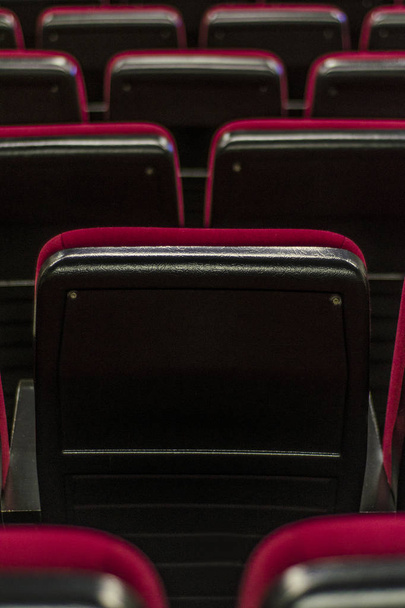 schönes und vielfältiges Thema. schöne Vintage-Sessel sind rot in weichen Stoffpolstern in einem Theater, Kino und anderen öffentlichen Räumen in einer Reihe vor dunklem Hintergrund. - Foto, Bild