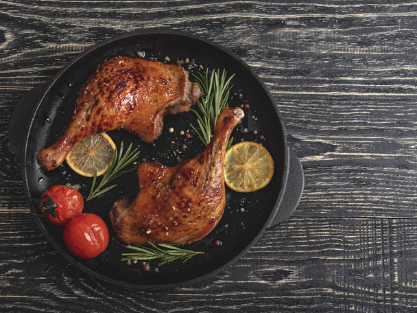 Juicy grilled duck legs with with tomato and lemon in a fry pan , black surface, close up - Foto, Imagem