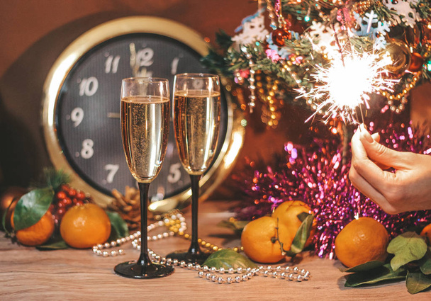 Christmas composition consisting of hours, the arrow of which is at 12 o'clock, glasses of champagne with bubbles, sparklers in the hand of a girl. - Foto, Bild