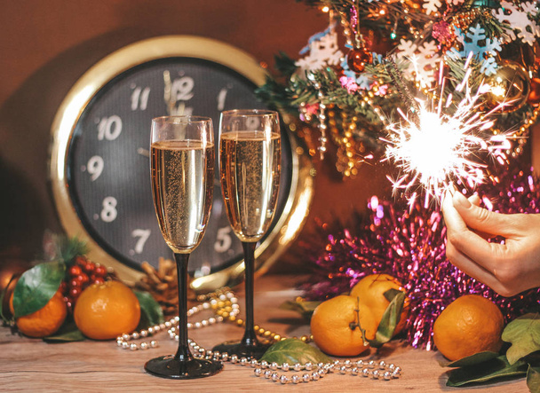 Christmas composition consisting of hours, the arrow of which is at 12 o'clock, glasses of champagne with bubbles, sparklers in the hand of a girl. - Photo, image