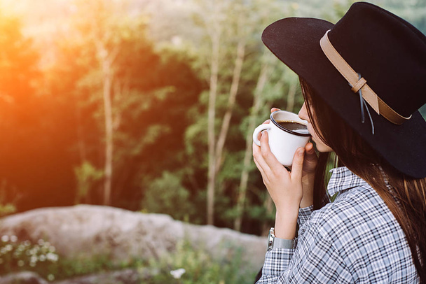 Beautiful girl in the hat drinks coffee on top of the mountain and enjoying the sunrise . Concept adventure active vacations outdoor in the mountains. Summer camp - Foto, immagini