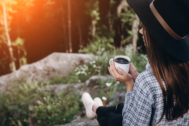 Beautiful girl in the hat drinks coffee on top of the mountain and enjoying the sunrise . Concept adventure active vacations outdoor in the mountains. Summer camp - 写真・画像