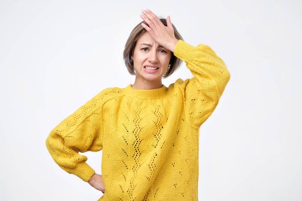 Portrait of excited young woman in yellow sweater holding her head - Photo, Image