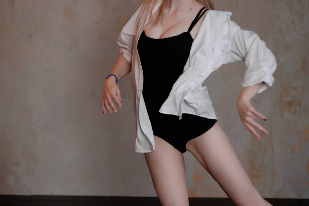 Beautiful slim young female modern jazz contemporary style ballet dancer wearing a black leotard and white shirt on a loft studio background - Zdjęcie, obraz