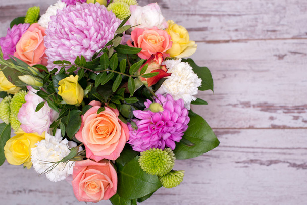 beautiful floral arrangement in the box, pink and yellow rose, pink eustoma, green and pink chrysanthemum, white carnation, dahlia on wooden background, top view, with space for text. - Photo, image