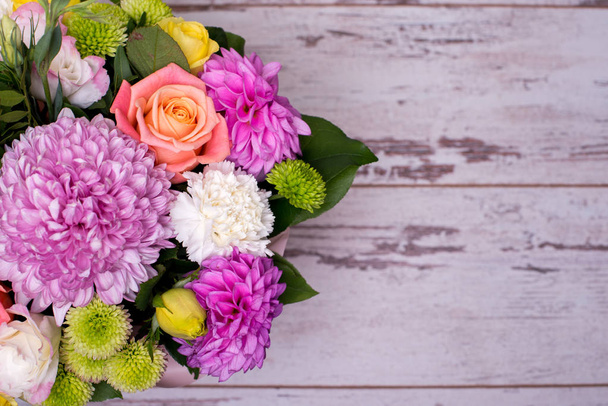 beautiful floral arrangement in the box, pink and yellow rose, pink eustoma, green and pink chrysanthemum, white carnation, dahlia on wooden background, top view, with space for text. - Фото, изображение