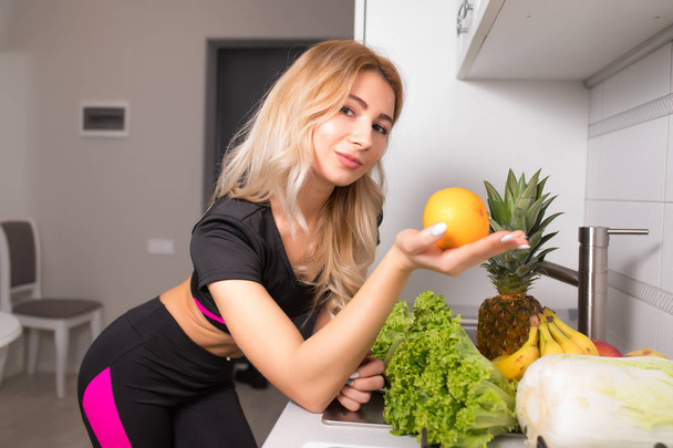 Sportive woman holding orange fruit on kitchen, healthy food diet concept - Фото, изображение