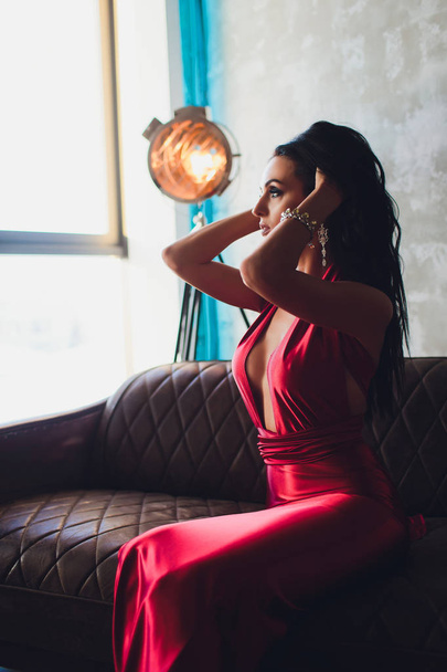 fashion studio photo of gorgeous woman with dark hair and evening makeup, wears luxurious red dress neon turquoise lights movie spotlight - Φωτογραφία, εικόνα