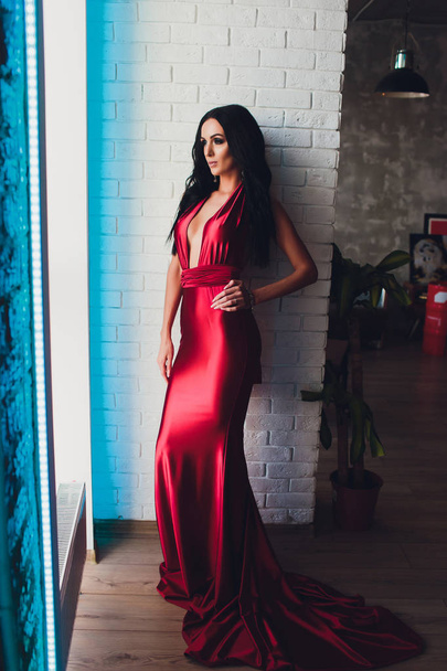 fashion studio photo of gorgeous woman with dark hair and evening makeup, wears luxurious red dress. neon turquoise lights - Photo, Image
