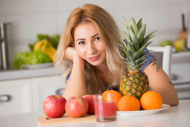 Pretty woman with fruits sitting at the table in kitchen, healthy food - Φωτογραφία, εικόνα