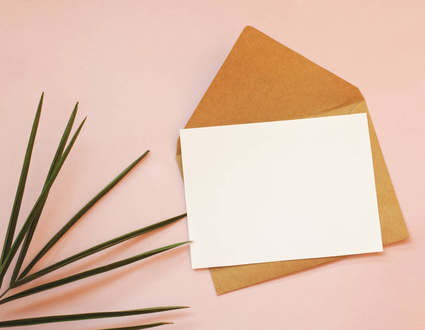 Конверт, белая пустая бумага и пальмовый лист на розовом фоне
. - Фото, изображение