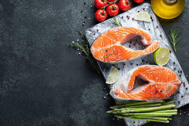 Two raw fresh salmon or trout steaks, rich in omega-3 oil, with lime, thyme and olive oil on a dark background. Healthy and dietary food. Top view with copy space. Flat lay. - Photo, Image