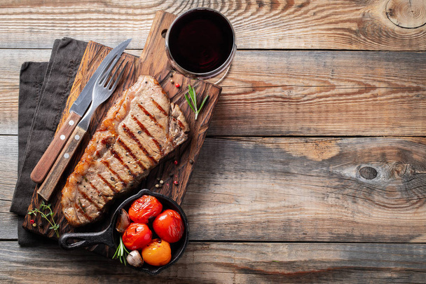 Steak Striploin, grilled with pepper, garlic, salt and thyme served on a wooden board. The finished dish for dinner with a glass of red wine on a old wooden rustic table. Top view with copy space. - Foto, afbeelding