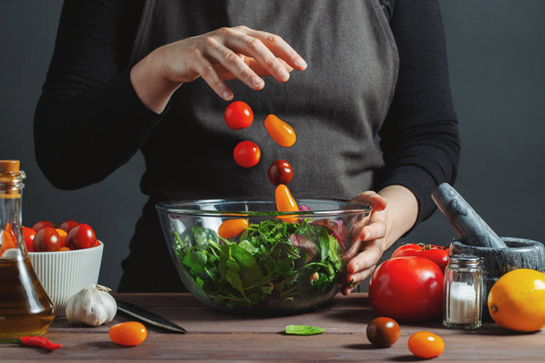 El chef vierte tomates cherry en un tazón. Frost en movimiento. Para preparar ensalada. Concepto de comida deliciosa y saludable, cocina. Sobre un fondo gris
. - Foto, Imagen
