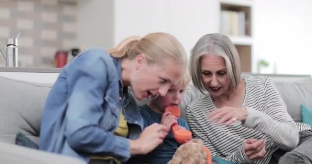 Child playing with a toy phone with mother and grandmother - Imágenes, Vídeo