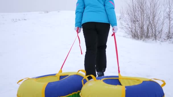 дівчина піднімається снігові гори і тягне сани і надувні сніг трубки. відпочинок в парк зими на різдвяні свята - Кадри, відео