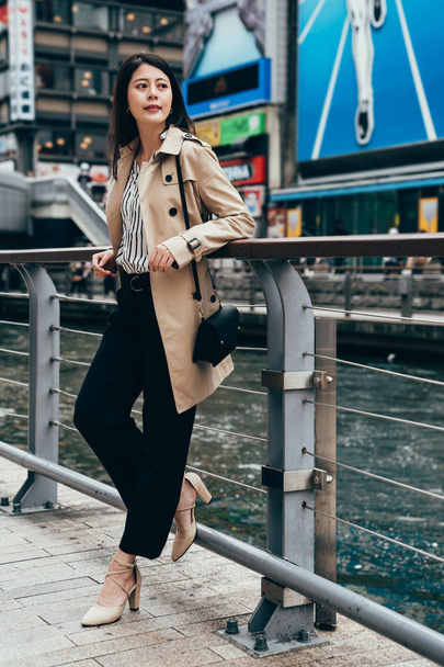 full length of fashion urban young woman living city lifestyle concept. female business worker after work relaxing near the river waiting for friends in famous runner nippon sign in dotonbori. - Foto, Bild