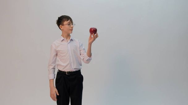 Um jovem de óculos e uma camisa branca está segurando uma maçã vermelha na mão e a examina. Espaço de cópia
. - Foto, Imagem