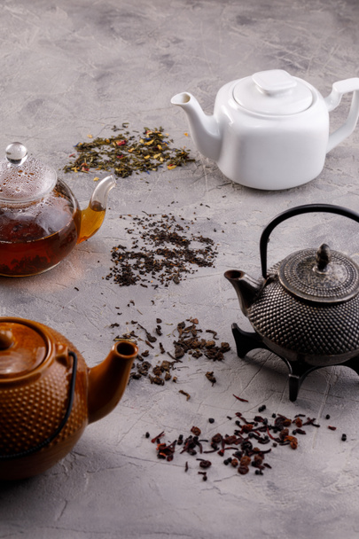 A variety of teapots with tea on a gray textured background. The concept of tea drinking. Close-up. - Фото, изображение