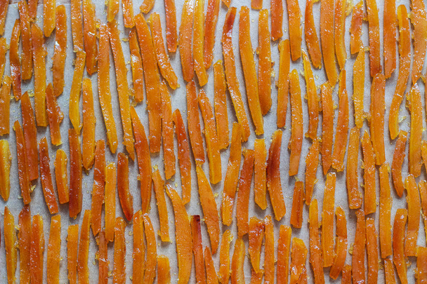 Консервированная апельсиновая кожура, приготовленная в сахарном сиропе с ванилью и имбирем, высыхающая на пергаменте. Селективный фокус
. - Фото, изображение
