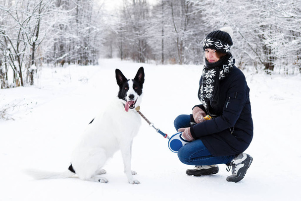 Beautiful young woman with her black and white dog on a walk in winter forest. - Foto, Imagem
