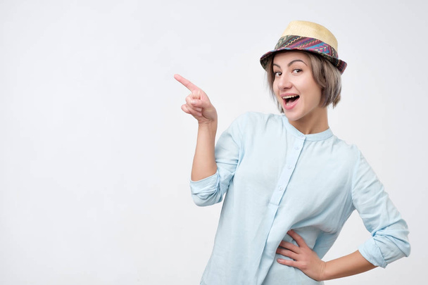 Jonge aantrekkelijke vrouw in zomer hoed en blauw shirt wijzen met haar vinger op copyspace - Foto, afbeelding