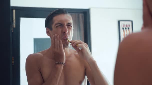 Portrait of man brushing his teeth in bathroom and stop becuse of a tooth pain. Dental problems - Materiał filmowy, wideo