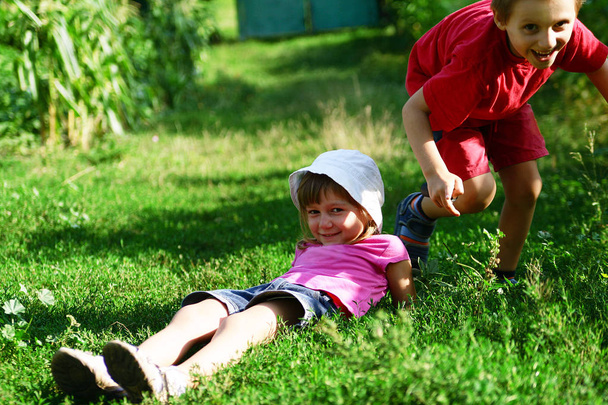子供は実行し、外夏の緑の草の上を再生します。少年と少女が草の上に横たわっていると笑って. - 写真・画像
