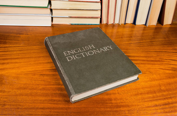 Gesloten van oude hardback Engels woordenboek met doek dekking op een houten tafel op een achtergrond van andere boeken - Foto, afbeelding