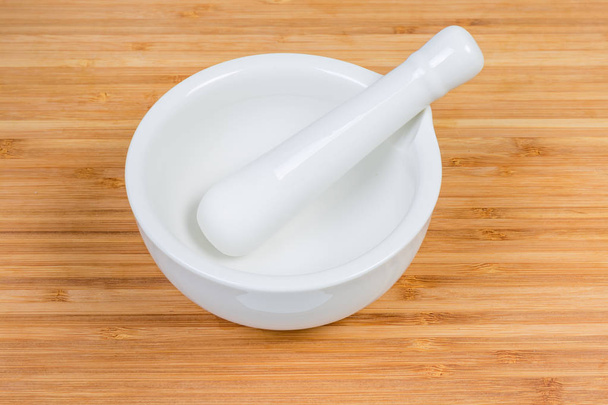 Пустой белый фарфоровый кухонный раствор с пестиком на бамбуковой деревянной доске
 - Фото, изображение