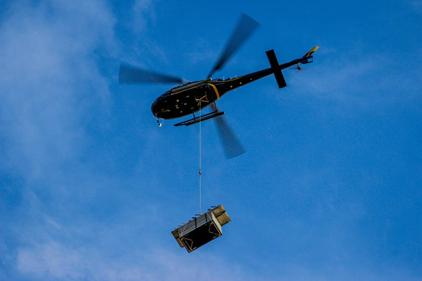 Helicóptero com lâminas desfocadas carregando cargas voando contra o céu azul
 - Foto, Imagem