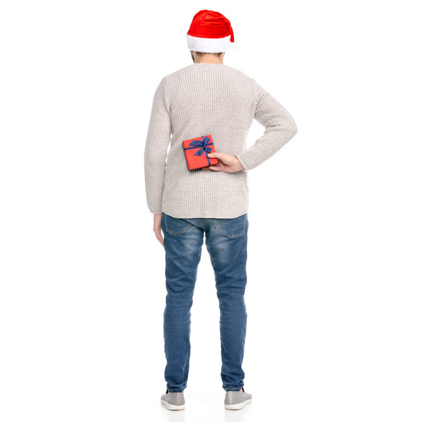A man in jeans sweater with Santa hat showing of positive emotions happy with box gift in hand - Фото, изображение