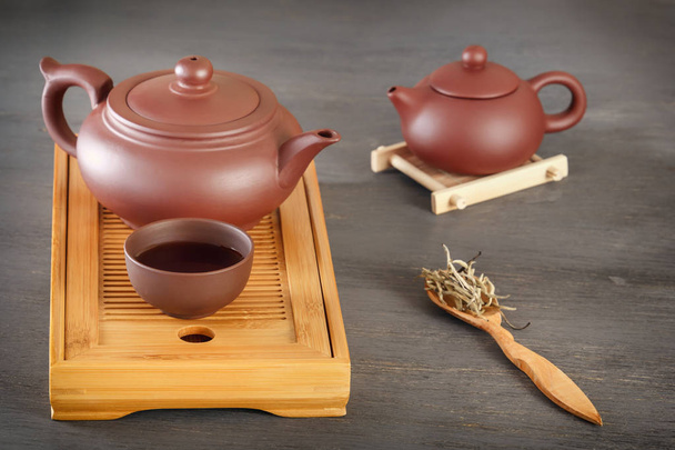 Традиційний азіатський керамічний чайник з чашкою стоїть на спеціальному дерев'яному чайному лотку на сірому столі
 - Фото, зображення