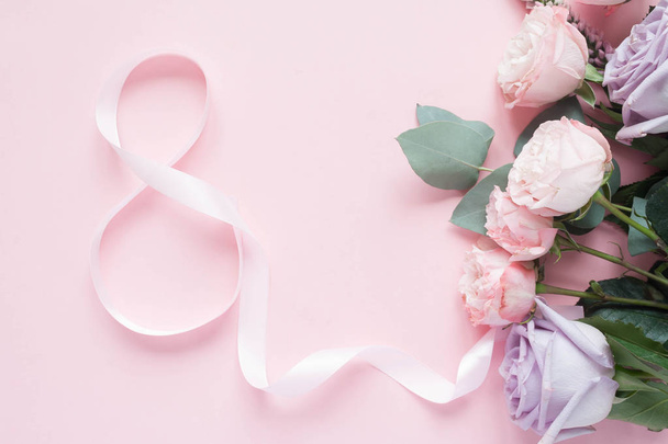 Frame of purple and pink roses, white Lisianthus and different flowers and pink ribbon in the shape 8 on pink background. Flat lay, top view - 写真・画像