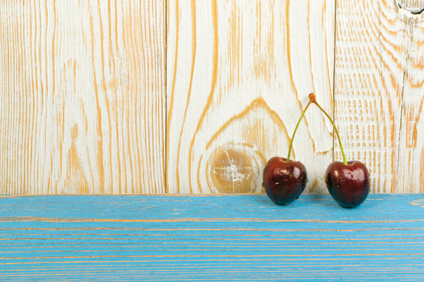 Two fresh ripe cherries on old wooden background for design montage. Blue wood table desk board with couple of overripe cherries or berries pair close up with copy space - Valokuva, kuva