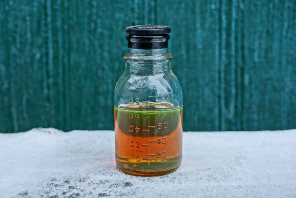 un liquide brun fermé provenant de l'huile moteur dans une bouteille en verre sur neige blanche sur fond vert
 - Photo, image