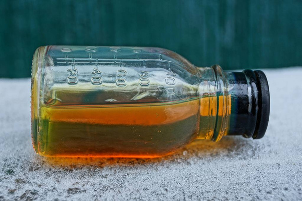 bruine vloeistof uit machine olie in een glazen fles op witte sneeuw op een groene achtergrond - Foto, afbeelding