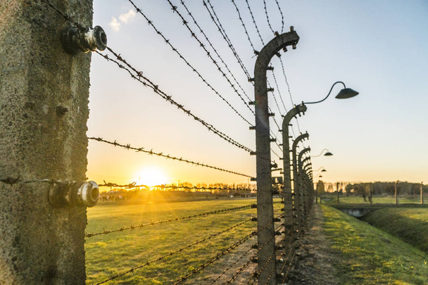 Barbed wire fence with lamps surrounding concentration camp at sunset in Auschwitz Birkenau, Poland - Photo, Image